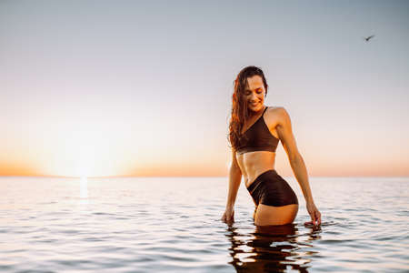 Young sporty woman in calm sea at sunset in black sportswear. Space for message.の写真素材