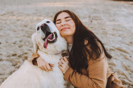 Beautiful young woman hugging with her golden retreiver dog on the beach at autumn warm day