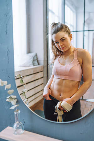 Beautiful fit woman with perfect abdominal muscles and obliques in front of mirror look at her...