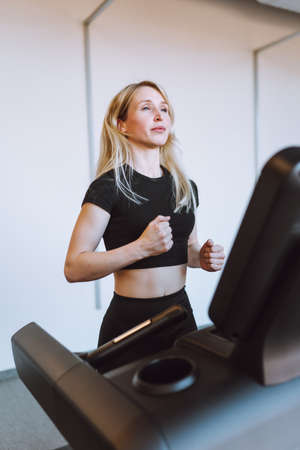 Attractive young blonde woman run on treadmill in fitness sport club. Fitness, cardio, weight lossの写真素材