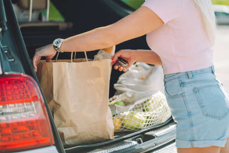 Unrecognizable woman put her shopping eco bags with food into car trunk on a parking.の写真素材