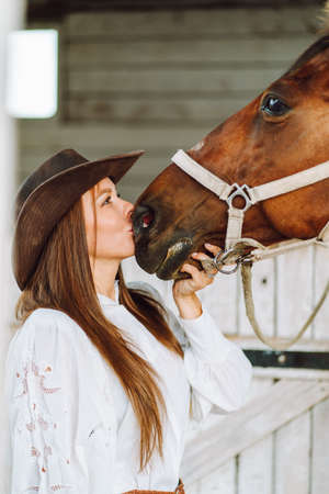Beautiful teenager girl in brown dress and brown horse standing near the door of wooden house
