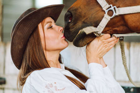 Beautiful teenager girl in brown dress and brown horse standing near the door of wooden houseの写真素材