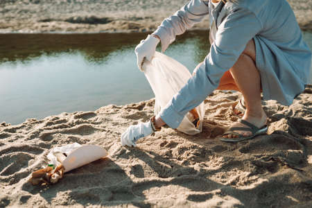 Woman collect plastic garbage on sandy beach of the sea. Spilled garbage on the beach. Environmental pollution conceptの写真素材