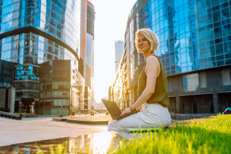 Blonde business woman wearing glasses sit with laptop among the skyscrapersの写真素材