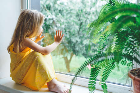 5 years old blonde girl staring out of the window on a wet cold rainy day.の写真素材