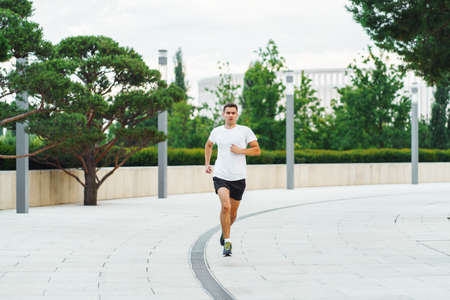 Attractive man athlete wearing sportswear run in modern park at summer dayの写真素材
