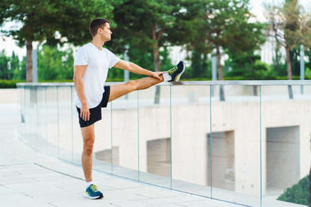 Attractive man athlete wearing sportswear do stretching exercises in modern park at summer morningの写真素材