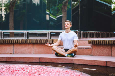 Attractive man athlete wearing sportswear meditate sitting in lotus pose in modern park at summer morningの写真素材
