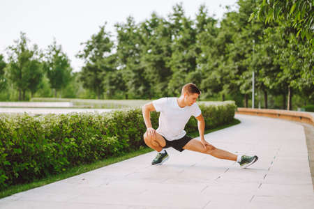 Attractive man athlete wearing sportswear do stretching exercises in modern park at summer morningの写真素材