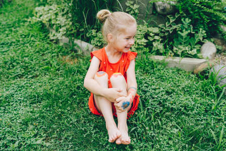 Smiling happy toddler girl wearing red dress sit on green grass barefoot.の写真素材