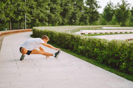 Attractive man athlete wearing sportswear do stretching exercises in modern park at summer morning