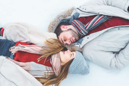 Top view of couple man and woman lie on the snow in winter clothes and look at each other with loveの写真素材