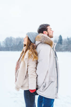 Young couple man and woman standing back to each other in winter snowy park with their eyes closed.の写真素材
