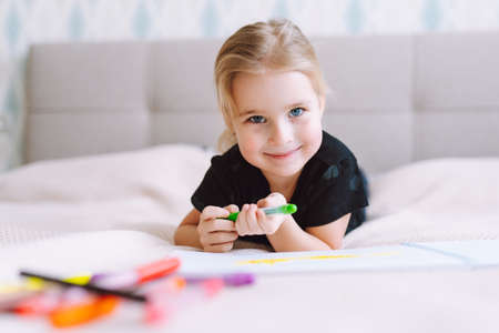 Blonde happy little girl drawing and writing with colorful pencils lying on bed at home and. Preschool education, early learningの写真素材