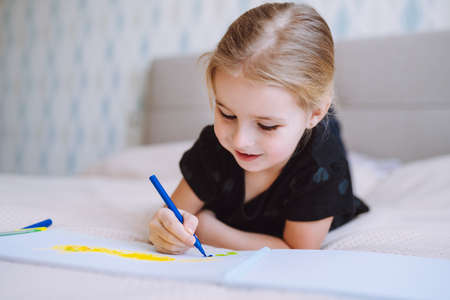 Blonde happy little girl drawing and writing with colorful pencils lying on bed at home and. Preschool education, early learningの写真素材
