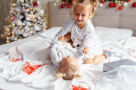 Two cute girls sisters play on bed at home in Christmas decorated room. Happy children, Christmas eveの写真素材