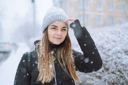 Outdoor portrait of young woman in warm jacket and knitted hat, turning her face to falling snowflakes. Winter, skin protection conceptの写真素材