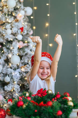 Santa little helper with decorative christmas tree on background. Little girl have funand express her emotions. Christmas and new year conceptの写真素材