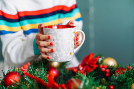Cropped image of little smiling girl holding christmas mug with hot chocolate and marshmallows with christmas wreath on background.の写真素材