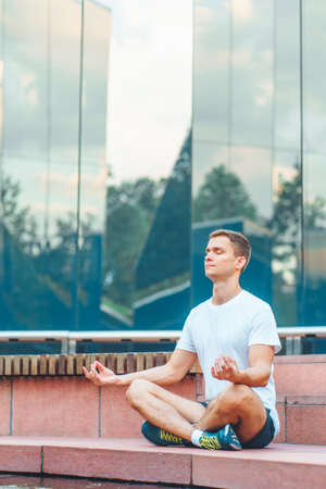 Attractive man athlete wearing sportswear meditate sitting in lotus pose in modern park at summer morning.の写真素材