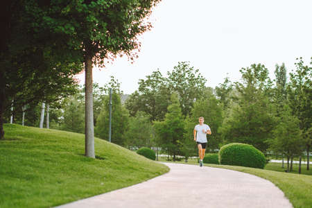 Attractive young man athlete wearing sportswear run in modern park at summer morning. Morning jogging, cardio, weight lossの写真素材