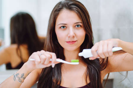 Close is portrait of young woman holding toothpaste and a toothbrush. Feemale look into camera and smile with a snow-white teethの写真素材