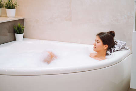 Young woman lies in white bath of foam with her eyes closed. Spa procedures, cleansing, relaxation,...
