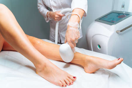 Laser epilation and cosmetology in beauty salon. Laser hair removal, skin care. Unrecognizable master do laser hair removal on womans legsの写真素材