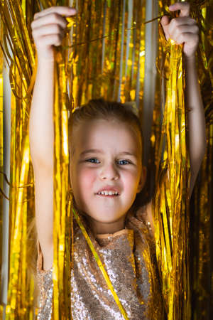 Cute blonde toddler girl wearing fancy dress smiling against golden glitter backgroundの写真素材