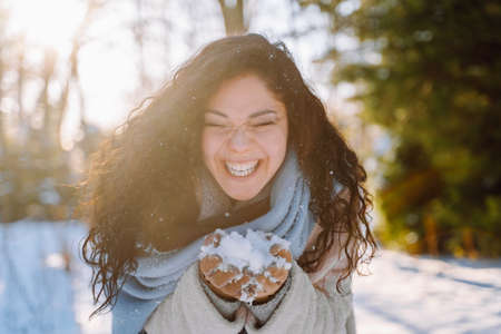 Smiling beautiful young woman have fun holding in hands snow wearing warm clothes and blue stole in winter forest.の写真素材