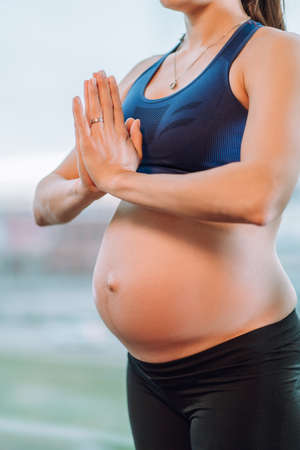 Young unrecognisable pregnant woman in sportswear stay and meditate and practice yoga on window background.の写真素材