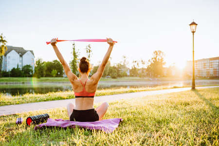 Young sportswoman do complex of stretch exercise before running in a park near the lake in the early summer morning.の写真素材