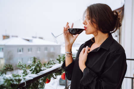 Side view of young woman with coiffured dark hair, make-up wear black shirt, standing on balcony...