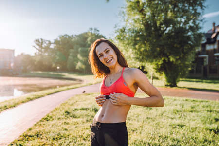 Cheerful woman in sportswear demonstrate press in green park near house in sunny day. Healthy lifestyle, sport activity, fitness outdoors. Useful training, morning relaxation, muscle pumping.の写真素材
