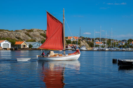 Marstrand, Sweden - September 5, 2014: Sailing boat with red sails cruises through the strait in Marstrand. Located in the archipelago north of Gothenburg Marstrand is a famous fishing village and tourist destination.のeditorial素材