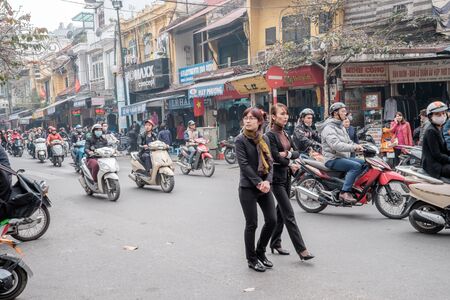 Hanoi, Vietnam - February 10, 2015: Vietnamese women cross the street with a slow and steady pace to...