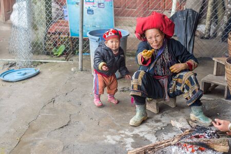 Sapa, Vietnam - February 13, 2015: Red Dao woman with a grandchild in a village outside Sapa. Sapa is famous for its rugged scenery and its rich cultural diversity. Red Dao people is one of many a colorful tribes.のeditorial素材