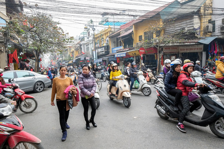 Hanoi, Vietnam - February 10, 2015: Vietnamese women cross the street through busy traffic in the old quarter of Hanoi. There are approximately four million motorbikes on the streets of Hanoi.のeditorial素材