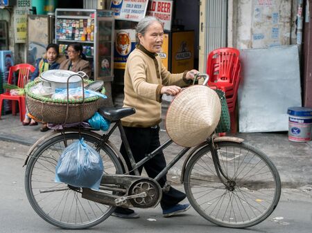 Hanoi, Vietnam - February 10, 2015: Vietnamese woman walks with a bike in the old quarter of Hanoi. The 36 old streets and guilds of the old quarter are a major tourist attraction.のeditorial素材