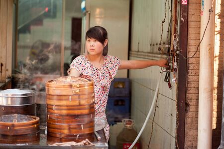 Xian China   June 20 2012: Young Hui woman steams dumplings at famous Muslim Street in Xian. Hui people are a Muslim ethnic minority in Xian and run a lively market at Muslim Street.のeditorial素材