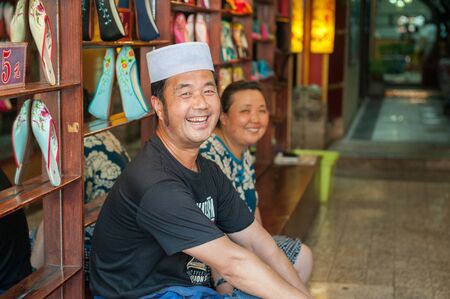 Xian China  June 20 2012: Laughing Hui shoe seller with wife at famous Muslim Street in Xian. Hui people are a Muslim ethnic minority in Xian and run a lively market at Muslim Street.のeditorial素材