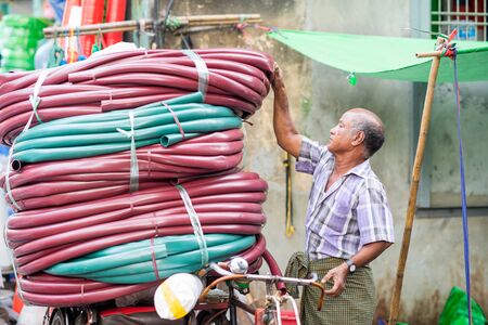 Yangon, Myanmar - February 10, 2014: Burmese man prepares a transport of tubing on a bicycle....