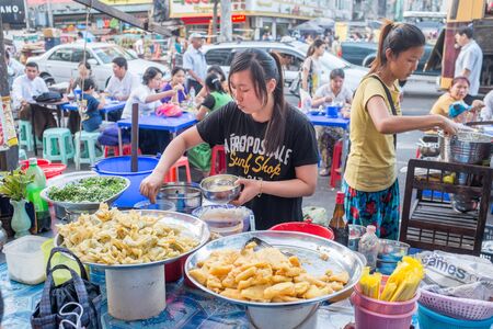 Yangon, Myanmar - February 5, 2014: Burmese people selling street food at the street market on Maha Bandoola Road in Chinatown. Myanmar is ethnically diverse with 51 million inhabitants belonging to 135 ethnic groups.のeditorial素材