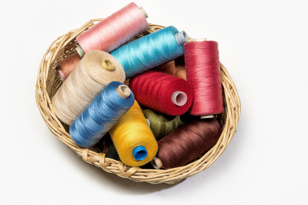 Still life of colorful spools of thread in a little basket on a white background - Closeup Detail -...