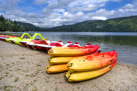 Stack of colorful yellow red rubber plastic canoes and a couple of pedal boats on an empty beach lake shore - concept activity water sports leisure vacation holiday adventure nature health bodyの写真素材