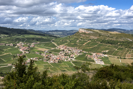 France, Saone-et-Loire, Solutre-Pouilly: Panoramic landscape view with French small town, famous Rock of Solutre on horizon, green vineyards, trees and cloudy blue sky - concept beauty nature travelの写真素材