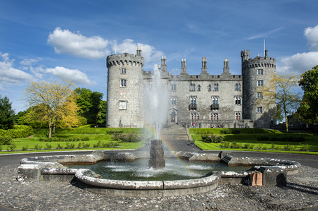 Ireland, Kilkenny: Park of the famous Castle of Butlers in the Irish town Kilkenny with water fountain rainbow green grass bushes people tourists residents and blue cloudy sky. June 10, 2015のeditorial素材