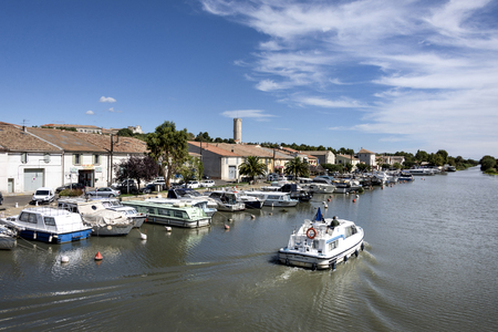 France, Gard, Saint Gilles: White yacht crosses harbor and Quay du Canal near city center of the French small town - concept water vacation fishing marina travel river leisure people. August 10, 2017のeditorial素材