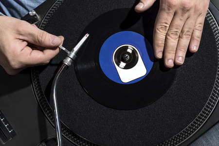 Two hands and a blue labeled single on a black record player